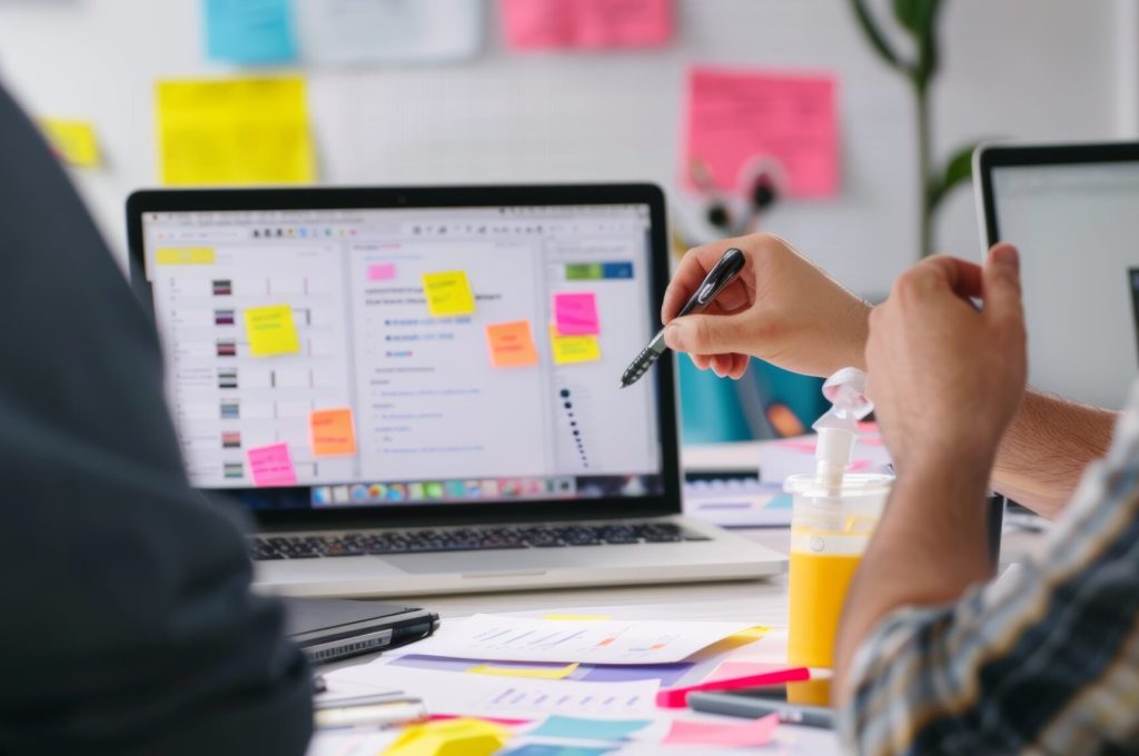 Marketing professionals engage in a collaborative discussion around a content calendar, featuring printed materials, graphs, and laptops on a wooden table. the teamwork setting focuses on strategic planning and digital marketing.